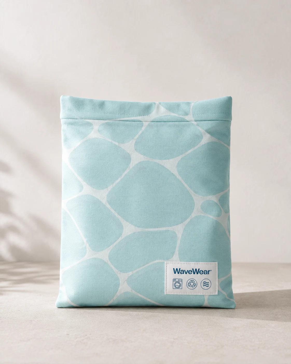 A soft seafoam fabric pouch printed edge to edge with the cell pattern, a small woven label at the lower right carrying the wordmark and three care icons